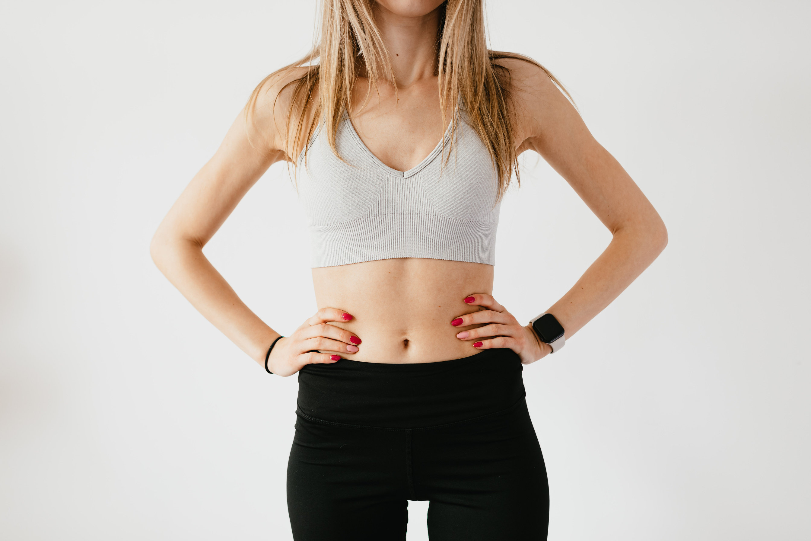Crop unrecognizable sportswoman in sportswear and smart watch near wall